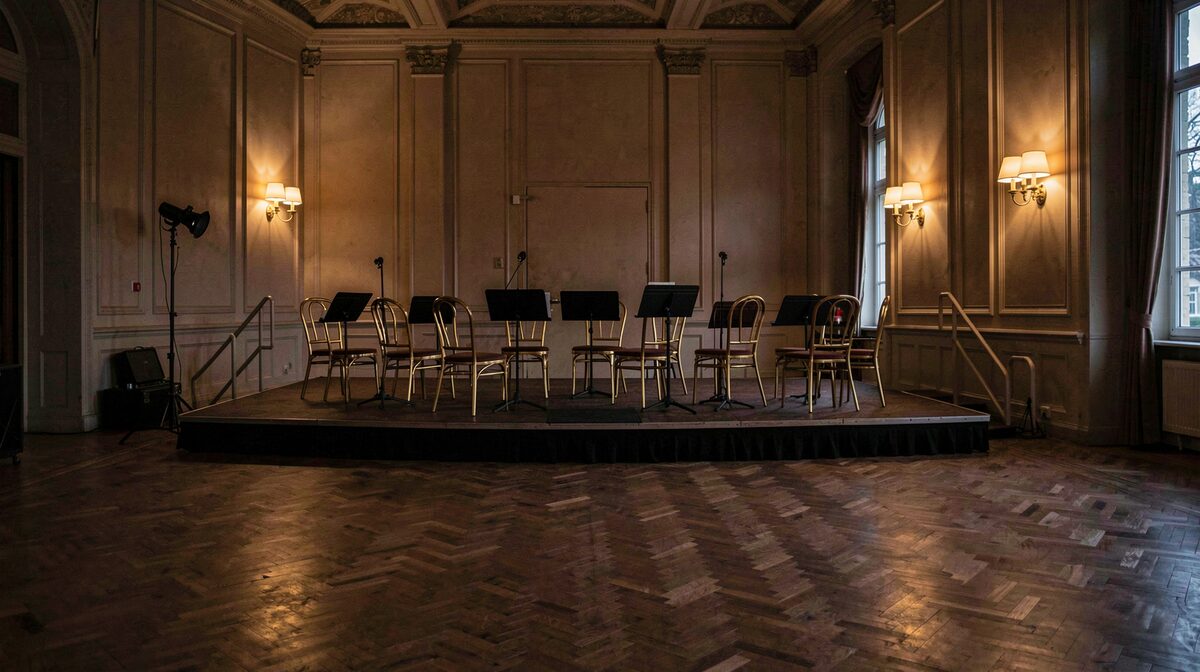 The empty bandstand of a heritage ballroom at dusk, brass section chairs arranged under warm wall sconces, parquet floor stretching into shadow.